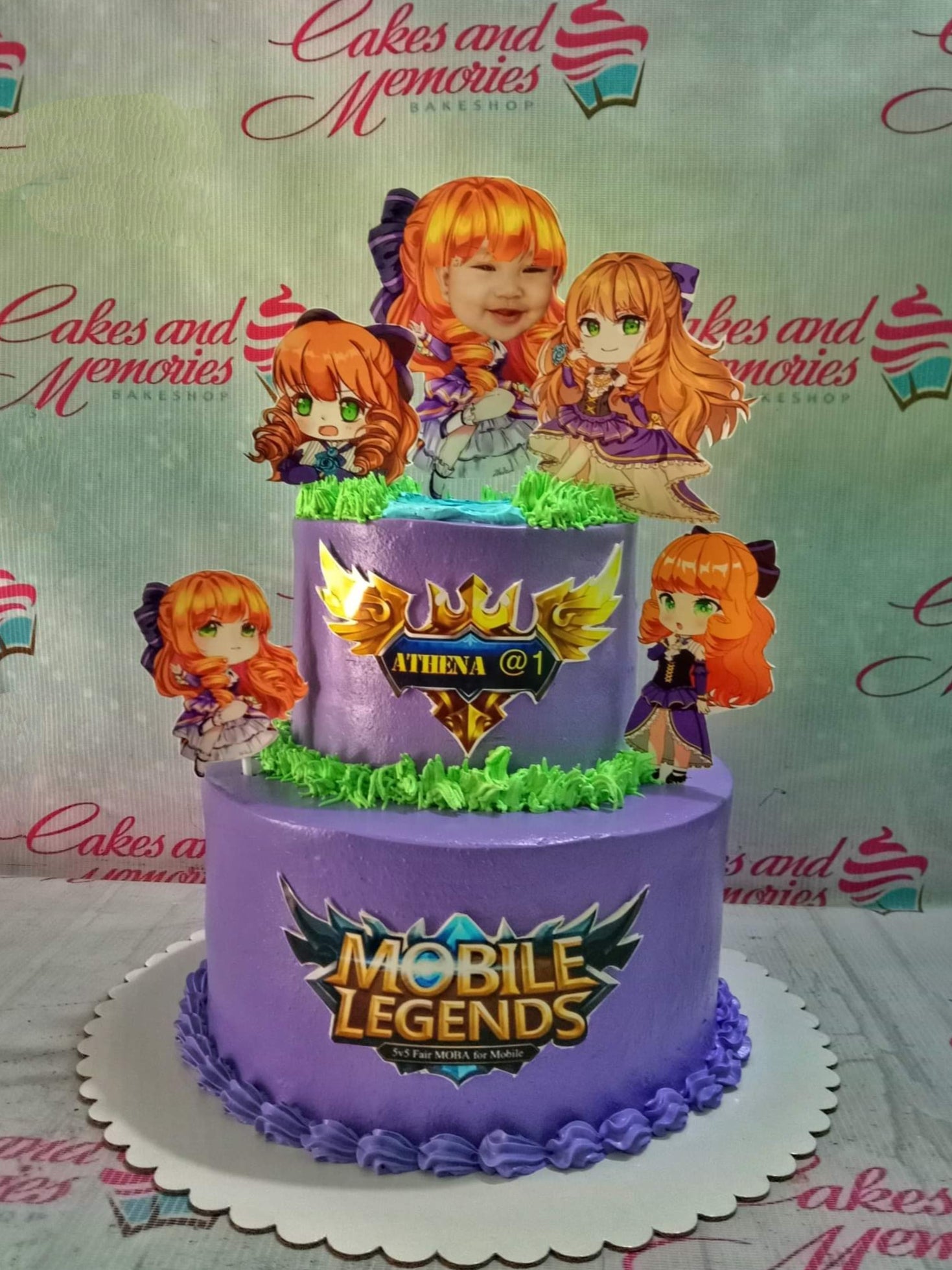 Two-tier purple Mobile Legends themed cake with anime character printouts and green icing grass accents. Two-tier purple Mobile Legends themed cake with anime character printouts and green icing grass accents.
