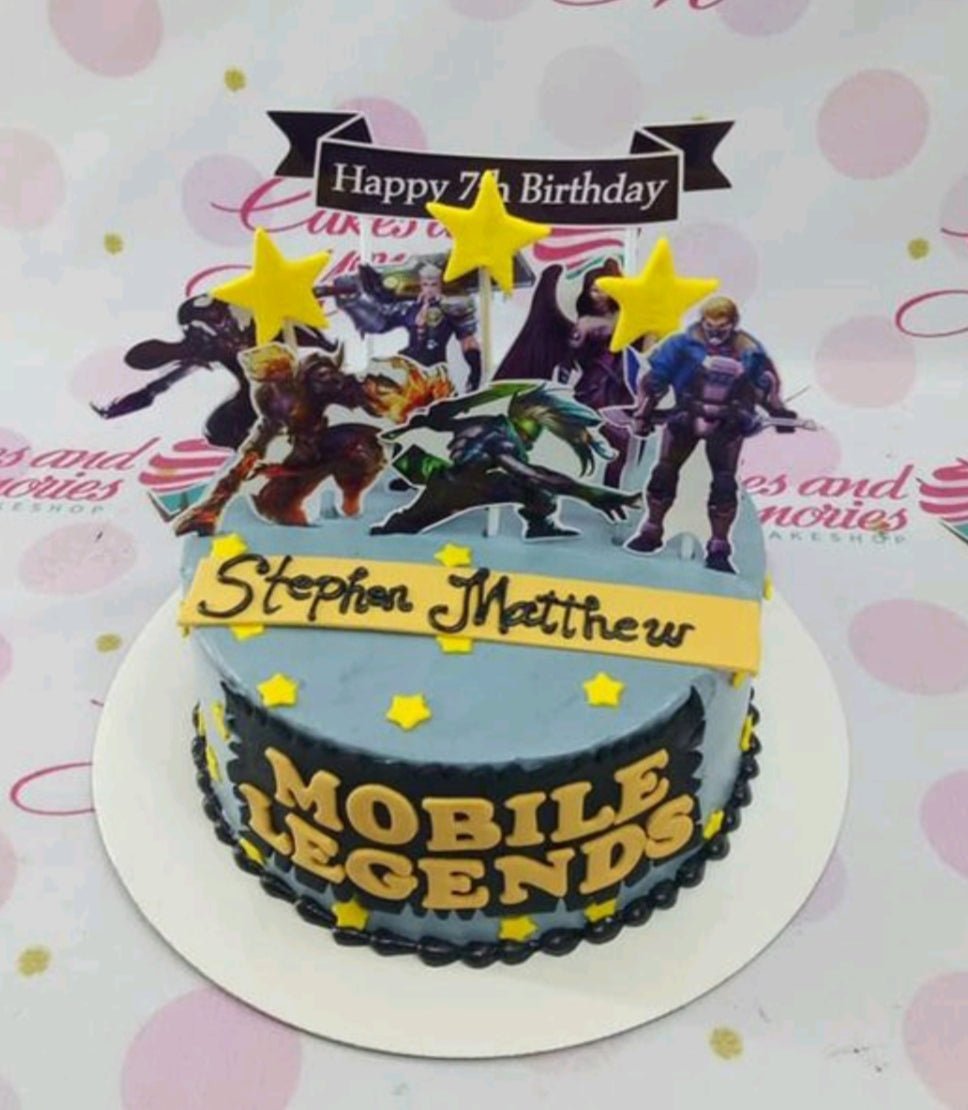 Mobile Legends themed birthday cake in light blue icing with character printouts, yellow stars, and a black banner topper. Mobile Legends themed birthday cake in light blue icing with character printouts, yellow stars, and a black banner topper.