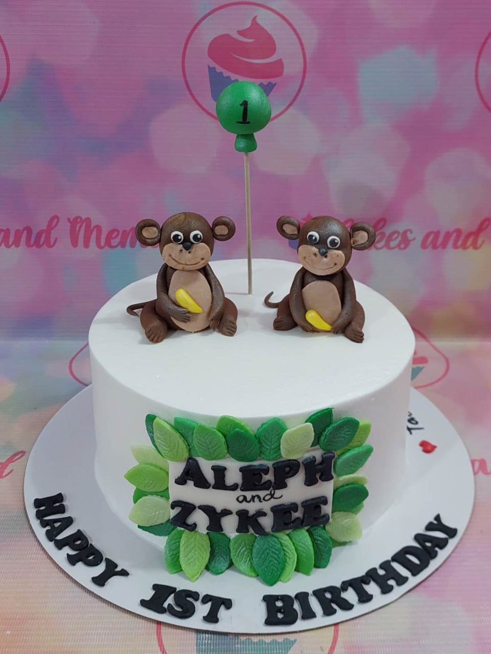 White 1-tier monkey themed birthday cake with two fondant monkeys holding bananas and green leaf decorations. White 1-tier monkey themed birthday cake with two fondant monkeys holding bananas and green leaf decorations.