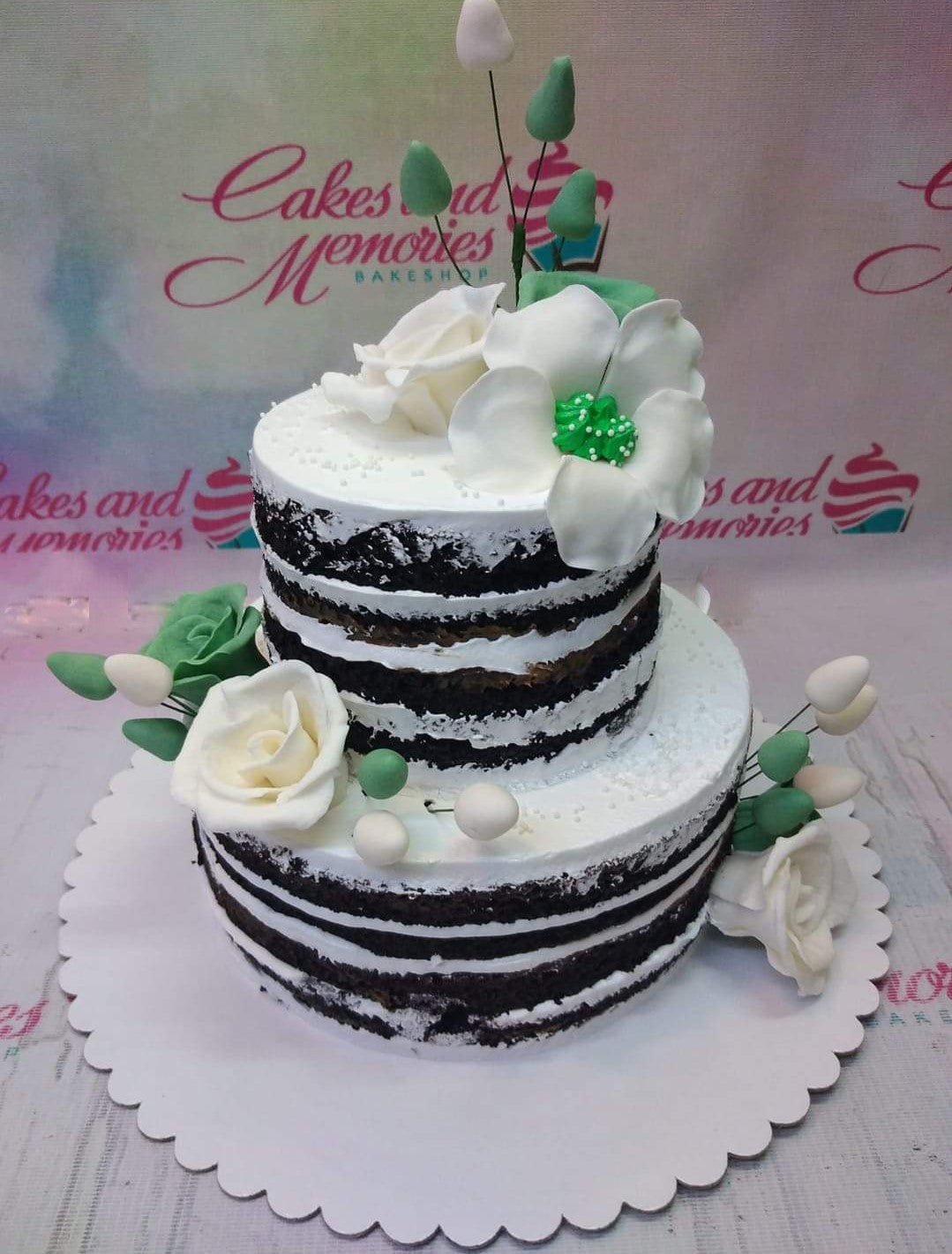Two-tier chocolate naked cake with white icing and white and green gumpaste flowers and buds. Two-tier chocolate naked cake with white icing and white and green gumpaste flowers and buds.