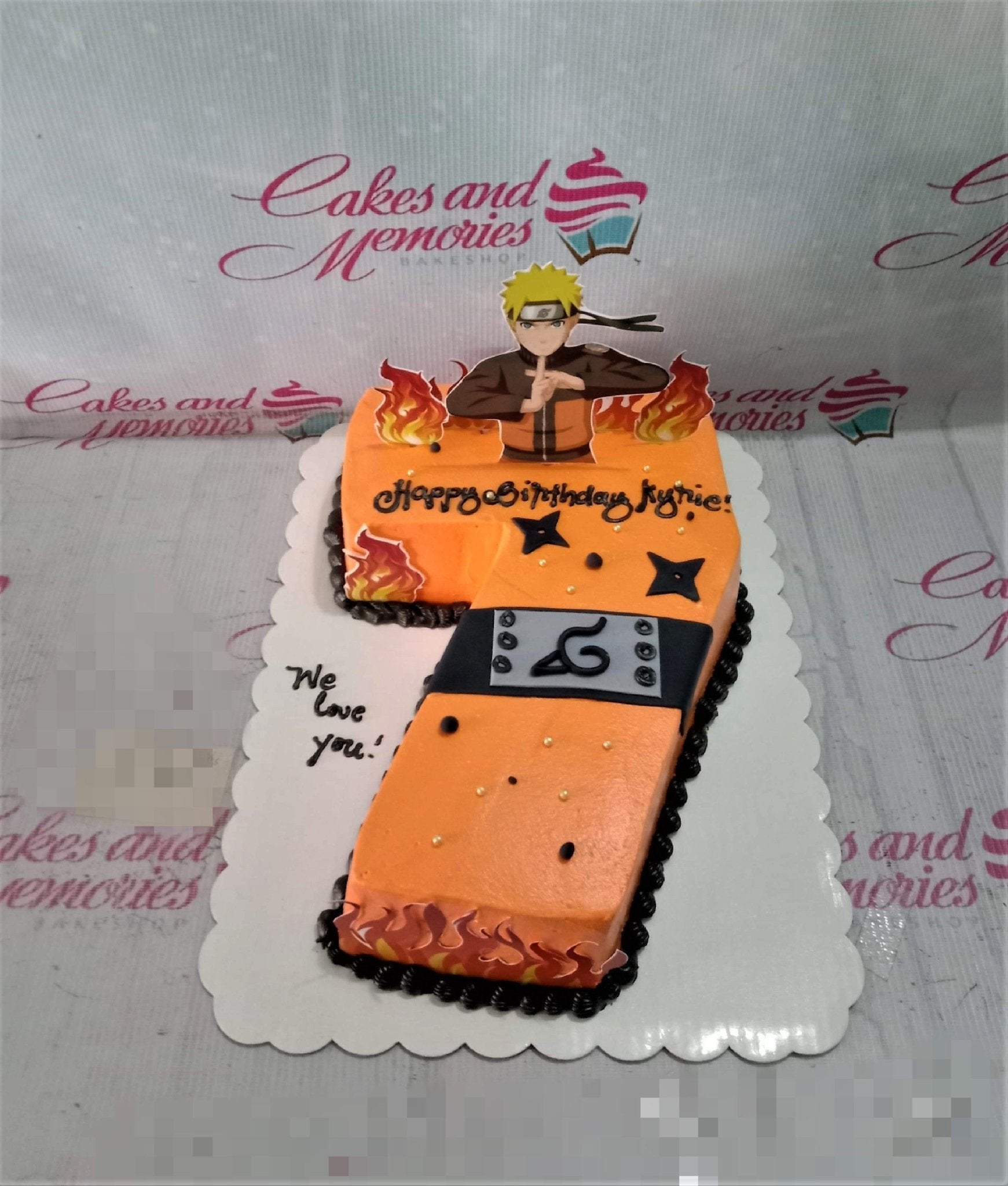 Orange Naruto themed number 7 shaped cake with character printouts, black icing borders, and flame decorations. Orange Naruto themed number 7 shaped cake with character printouts, black icing borders, and flame decorations.