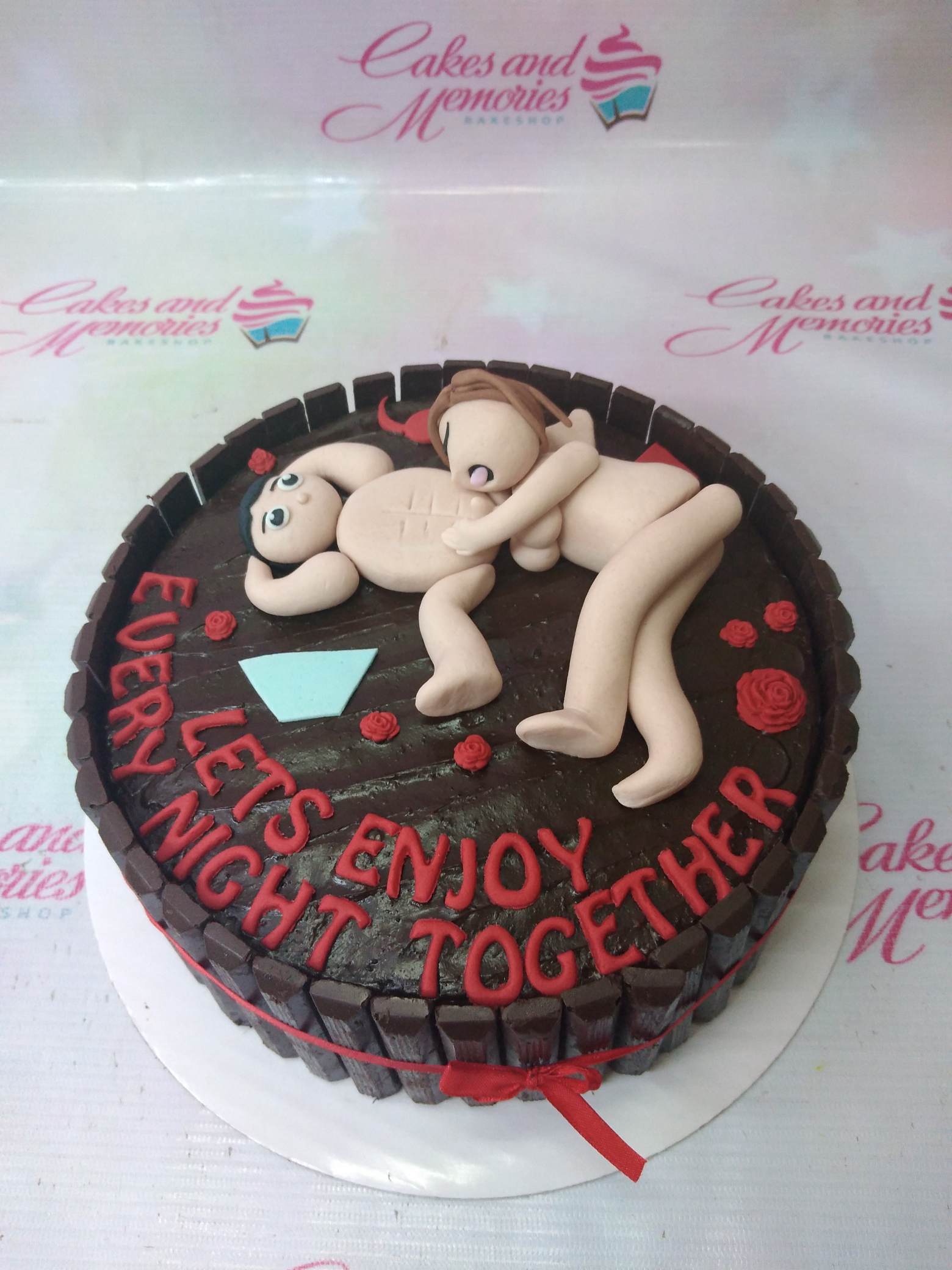 Chocolate cake with 3D fondant figures of a couple in bed, red icing roses, and KitKat chocolate bar border. Chocolate cake with 3D fondant figures of a couple in bed, red icing roses, and KitKat chocolate bar border.