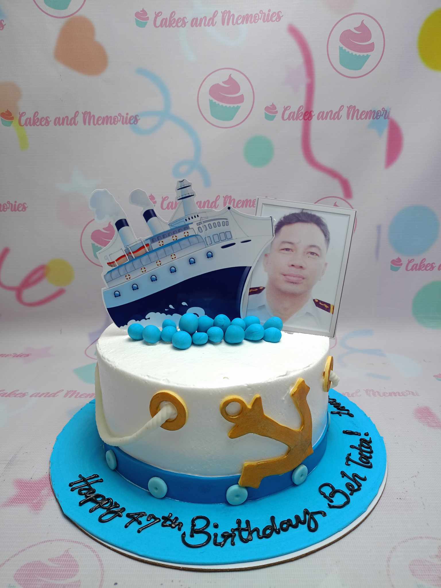 White nautical themed birthday cake with a cruise ship printout, a photo topper, and gold anchor decorations on a blue base board. White nautical themed birthday cake with a cruise ship printout, a photo topper, and gold anchor decorations on a blue base board.