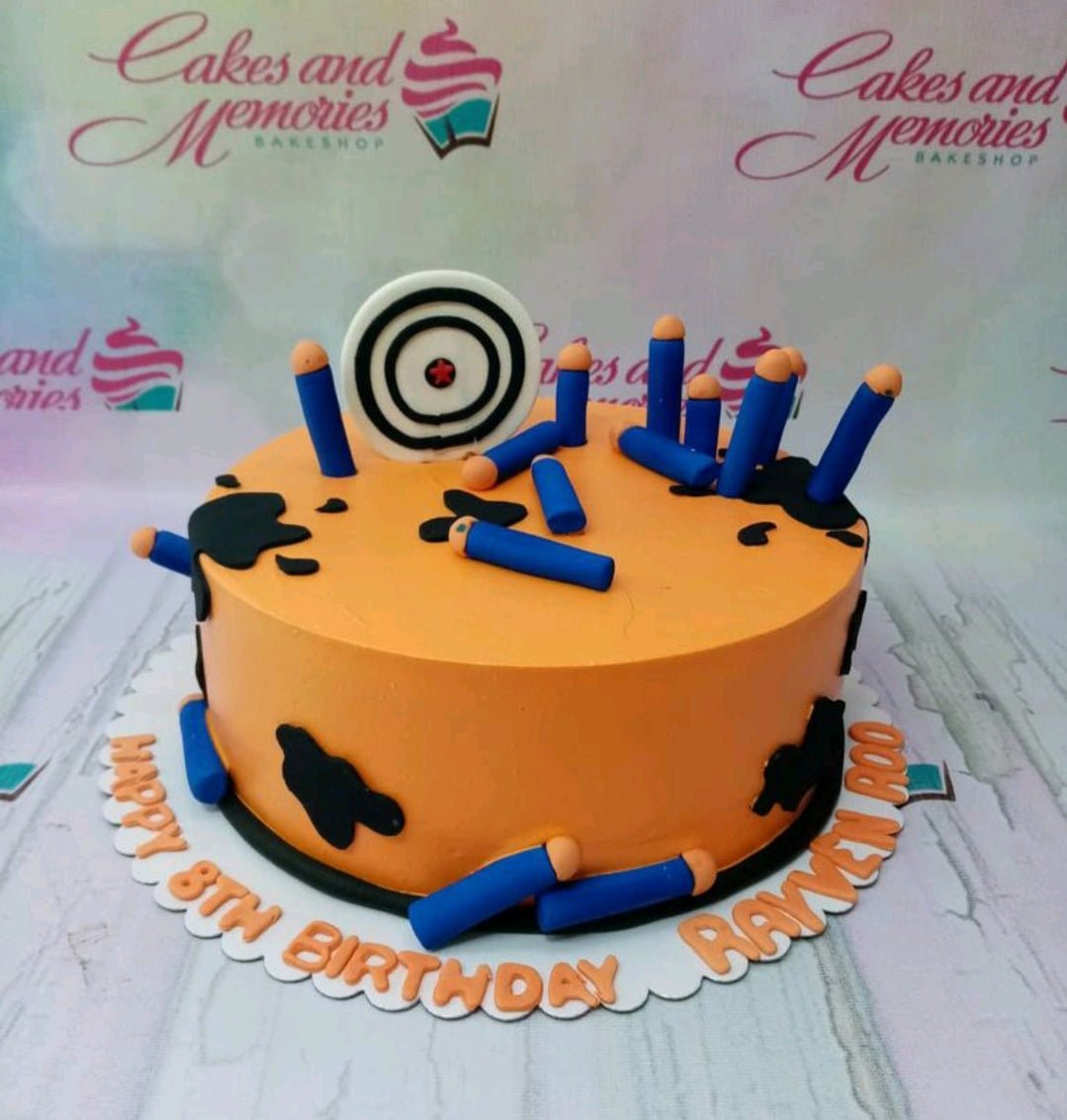 Orange Nerf themed birthday cake with blue dart toppers, black splat designs, and a target board topper. Orange Nerf themed birthday cake with blue dart toppers, black splat designs, and a target board topper.
