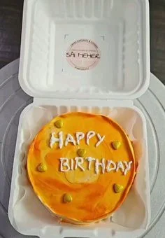 Orange and yellow marbled bento cake with white piped Happy Birthday message and gold heart accents in a white box. Orange and yellow marbled bento cake with white piped Happy Birthday message and gold heart accents in a white box.