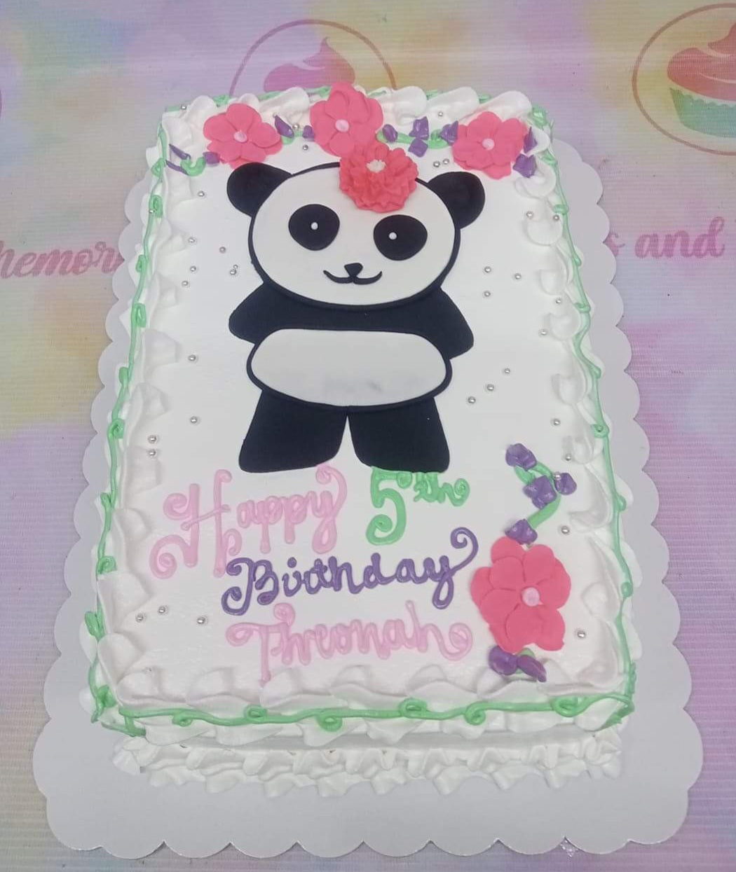 White rectangular panda birthday cake with pink icing flowers, purple vines, and silver dragees. White rectangular panda birthday cake with pink icing flowers, purple vines, and silver dragees.