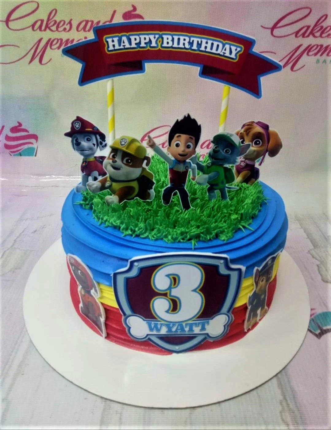 A multicolor 1-tier Paw Patrol cake, featuring character printouts, Happy Birthday banner, and green grass icing. A multicolor 1-tier Paw Patrol cake, featuring character printouts, Happy Birthday banner, and green grass icing.