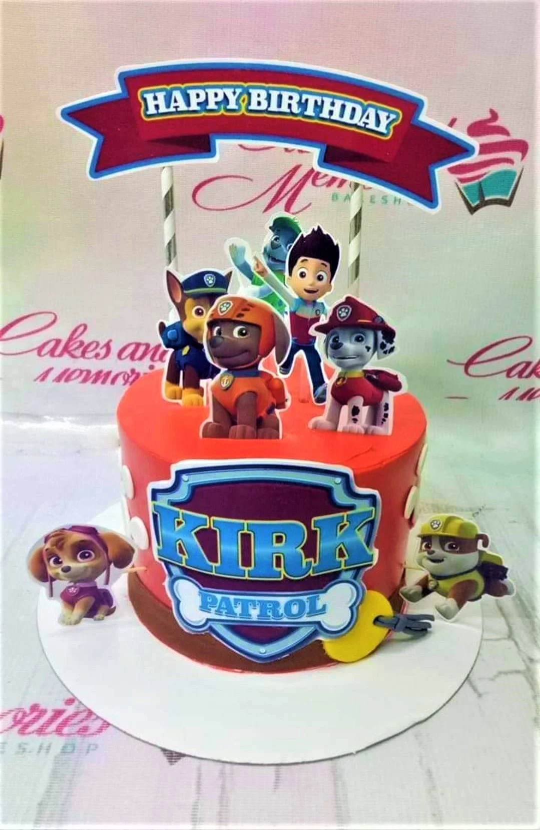 Paw Patrol-Inspired Coral Birthday Cake A red, blue, and yellow 1-tier cake themed around Paw Patrol, featuring Ryder, pups, and a custom 'Kirk' shield.