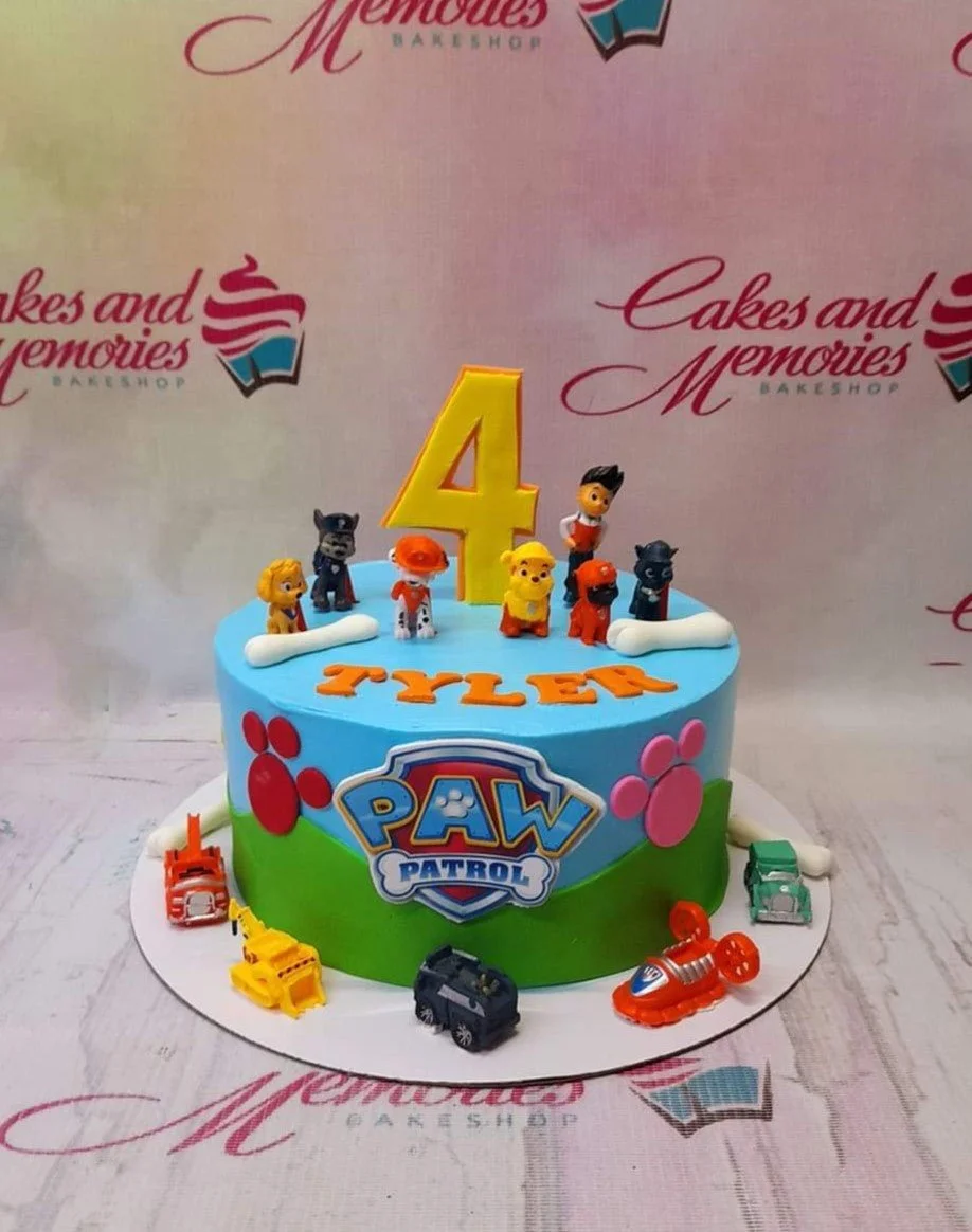 Paw Patrol-Inspired Birthday Cake A blue and green 1-tier Paw Patrol cake with toy pup figurines, a large yellow number 4, and toy rescue vehicles.