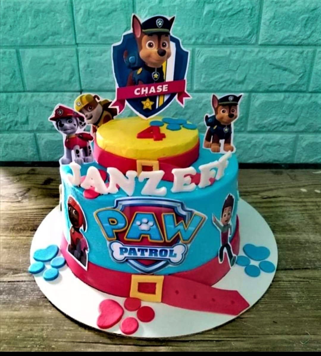 Two-tier blue and yellow Paw Patrol themed birthday cake with Chase and Marshall character toppers and red fondant belt accents. Two-tier blue and yellow Paw Patrol themed birthday cake with Chase and Marshall character toppers and red fondant belt accents.