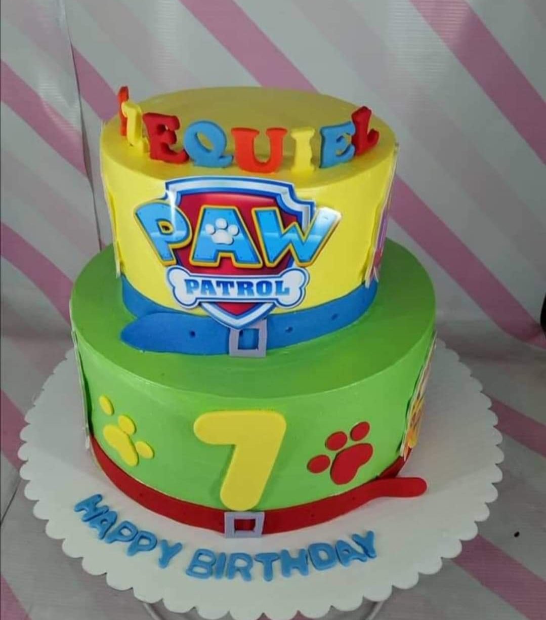 Two-tier Paw Patrol themed birthday cake with yellow and green icing, featuring character printouts and a large yellow number seven. Two-tier Paw Patrol themed birthday cake with yellow and green icing, featuring character printouts and a large yellow number seven.