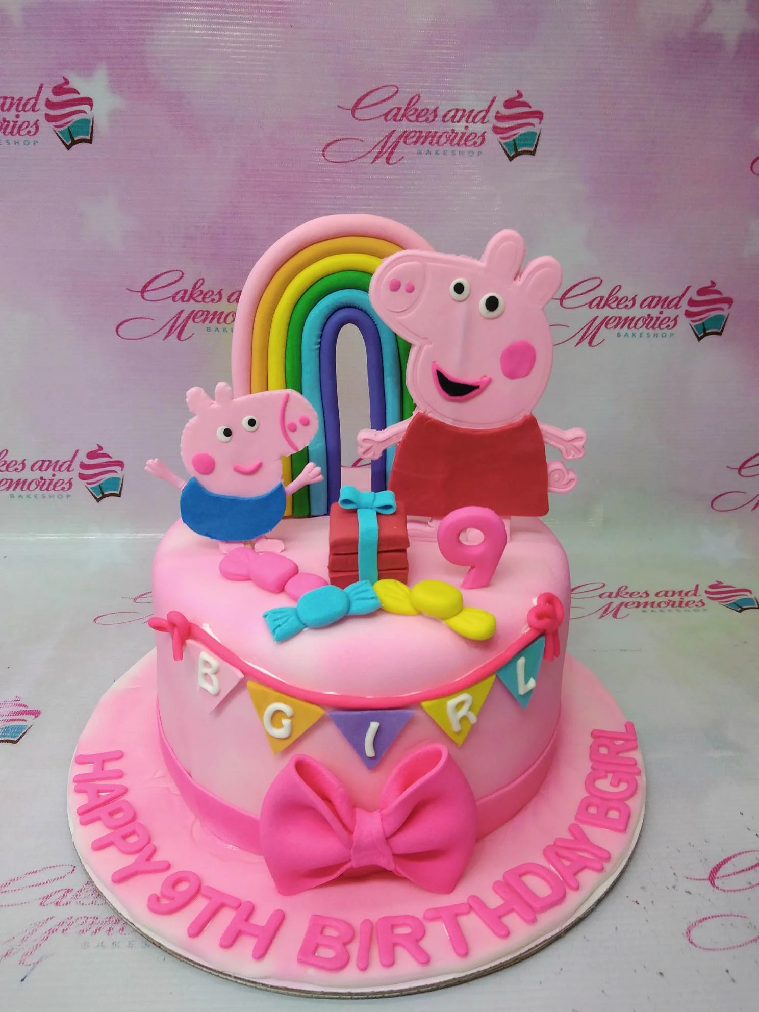Pink Peppa Pig themed fondant cake with a rainbow, George Pig, and a pink bow on a pink base board.