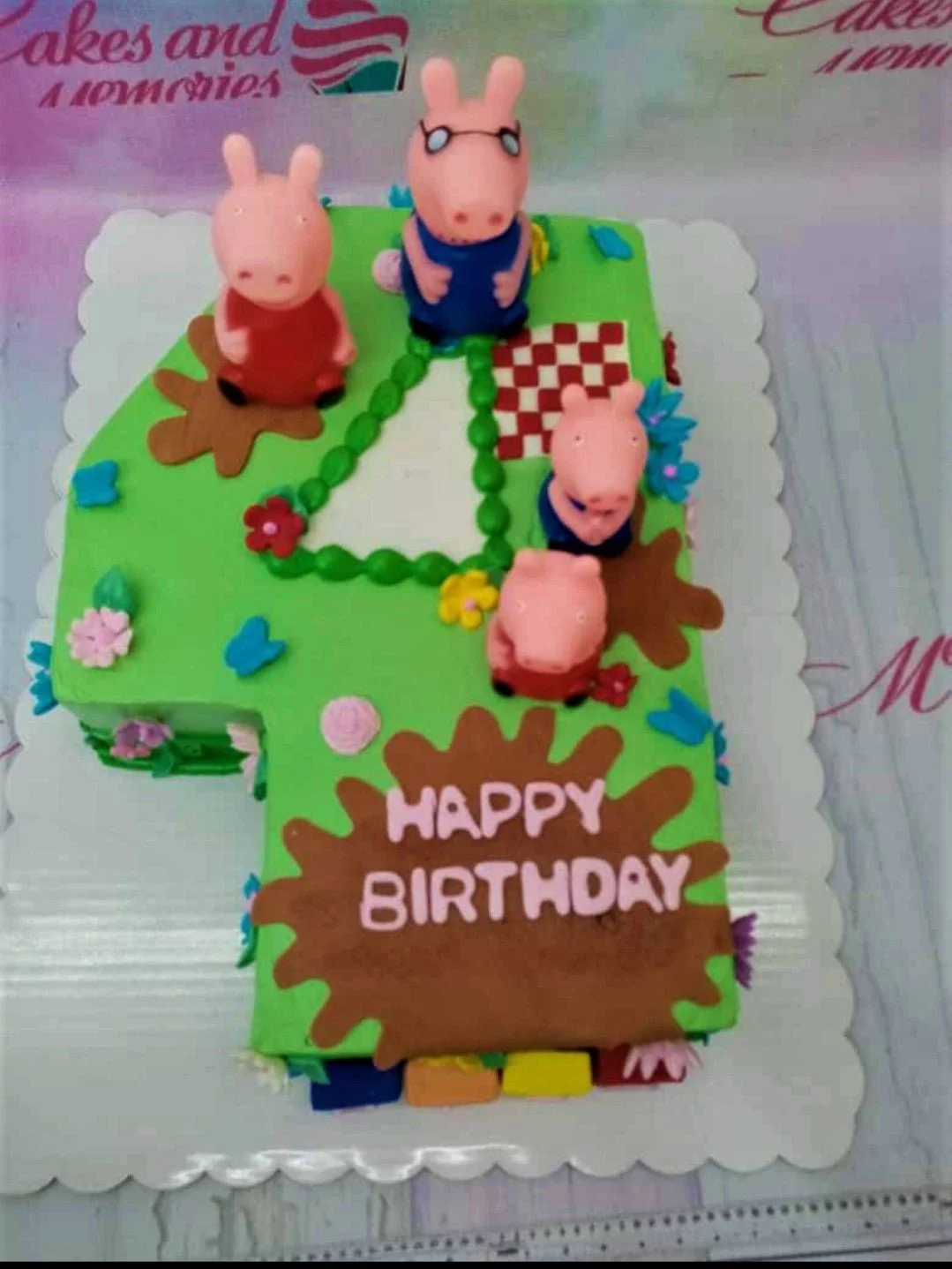 Peppa Pig themed number 4 shaped cake in green icing with fondant pig figurines and mud puddle decorations.