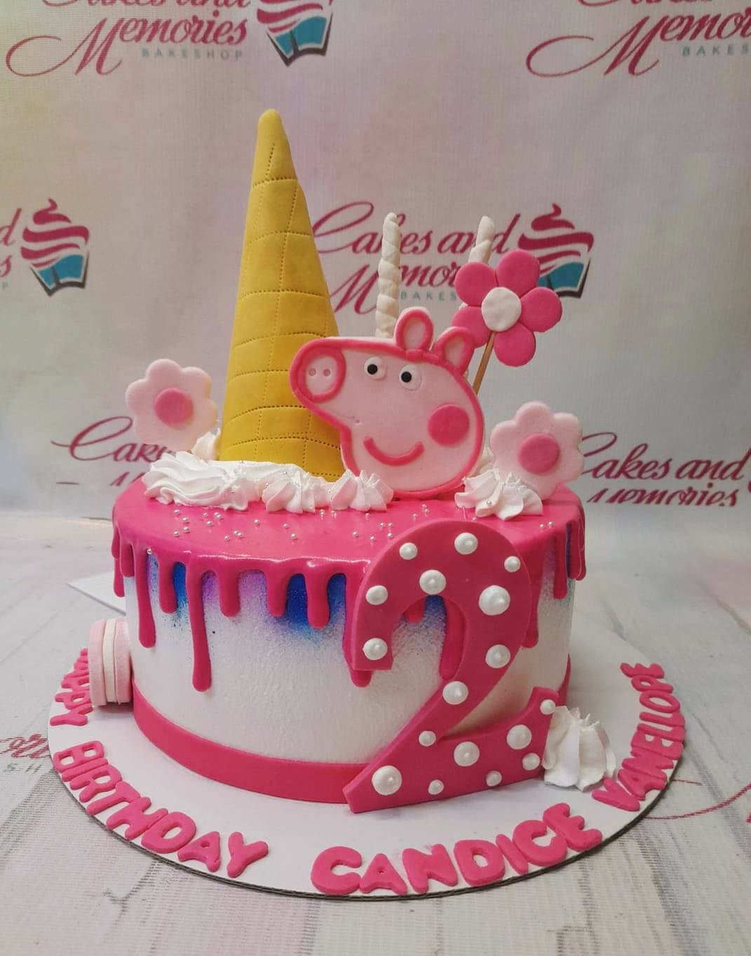 Peppa Pig themed birthday cake with pink drip, a yellow cone, fondant flowers, and a large pink number 2 on a white base. Peppa Pig themed birthday cake with pink drip, a yellow cone, fondant flowers, and a large pink number 2 on a white base.