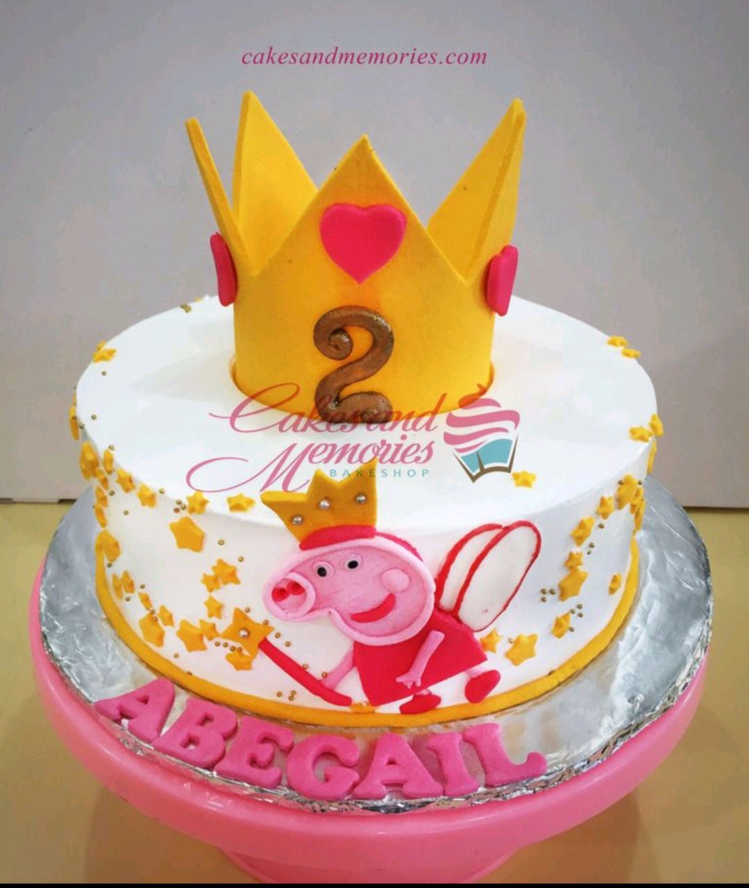 White 1-tier Peppa Pig birthday cake with a large yellow fondant crown, pink hearts, and gold stars. White 1-tier Peppa Pig birthday cake with a large yellow fondant crown, pink hearts, and gold stars.