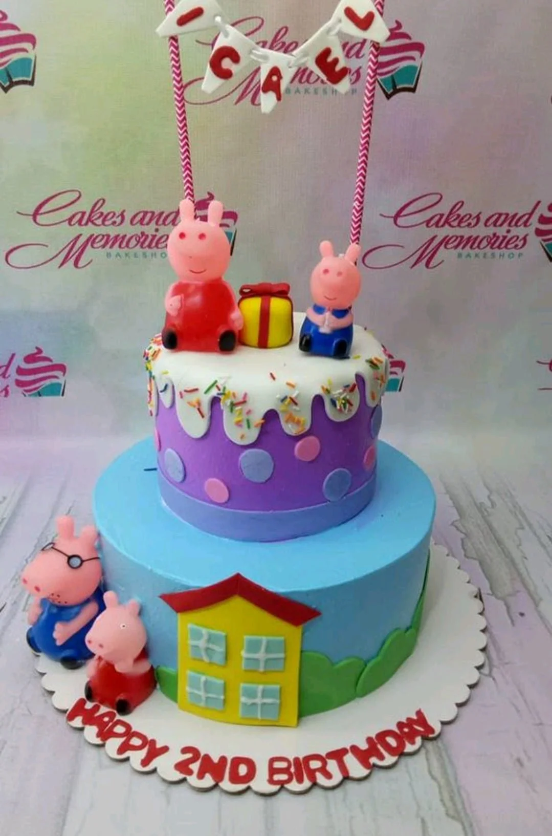 Two-tier Peppa Pig themed birthday cake with purple and blue icing, fondant house, and character figurines.