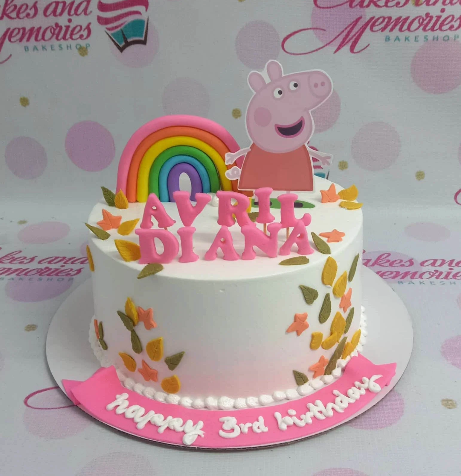White Peppa Pig birthday cake with a fondant rainbow, pink name letters, and colorful autumn leaves.