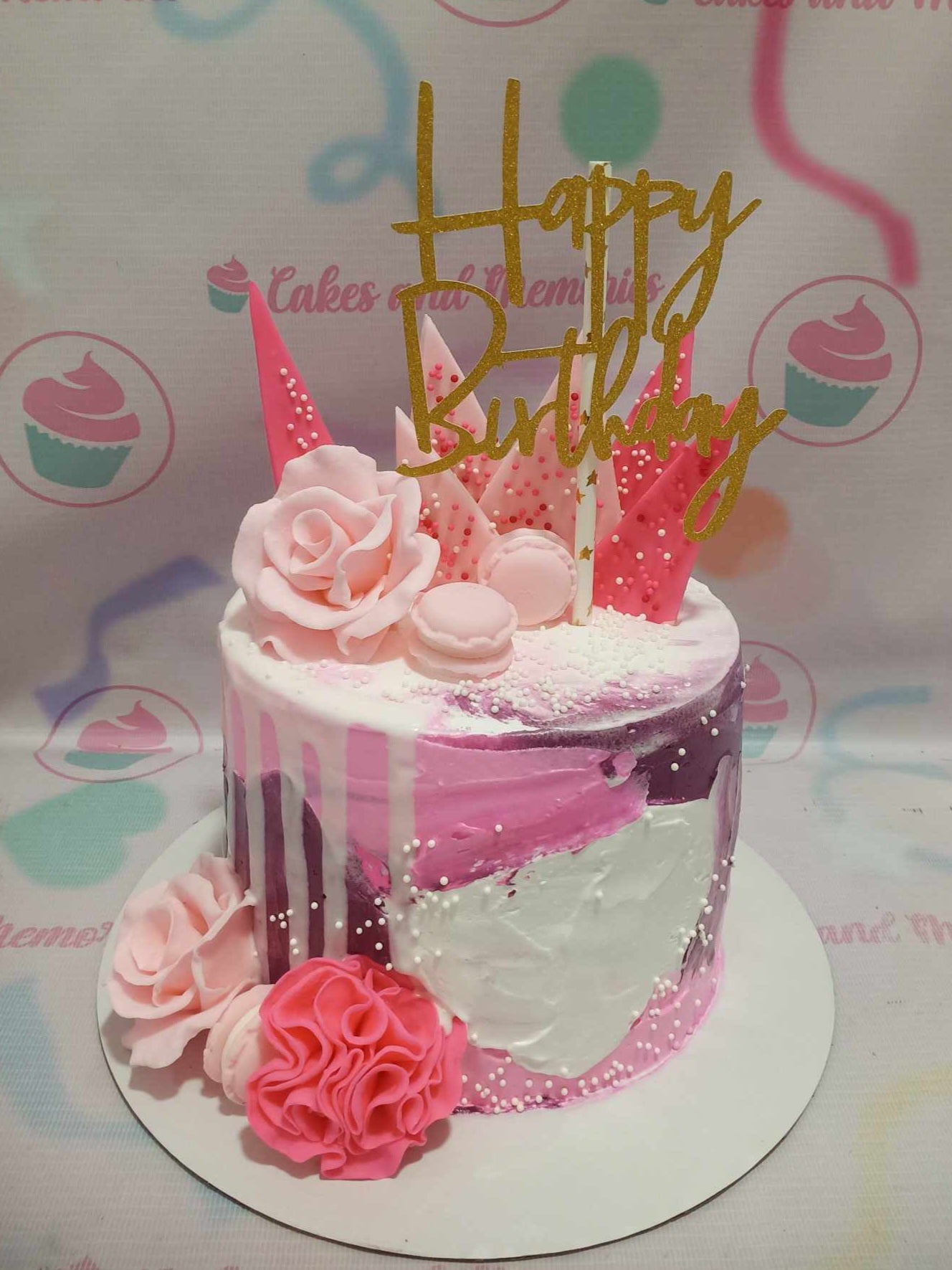 Pink and purple abstract palette knife cake with pink fondant roses, macarons, and a gold glitter Happy Birthday topper.