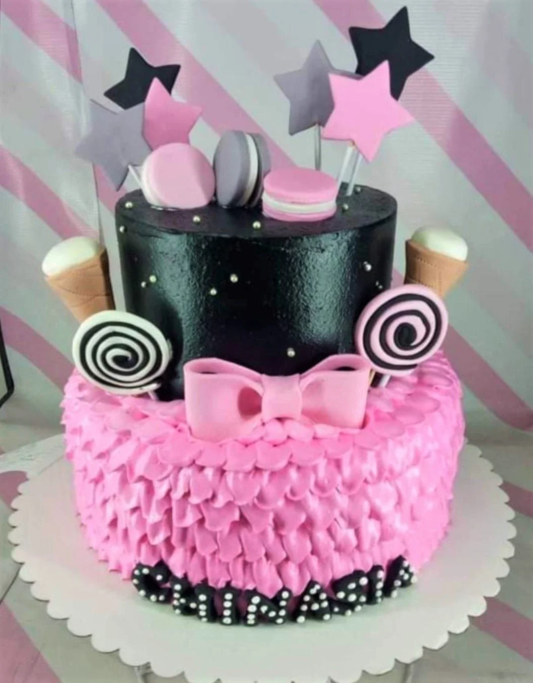 Pink Black Ruffle Bow 2-Tier Cake Two-tier pink and black cake with pink icing ruffles, black top tier, pink bow, macarons, and star toppers.