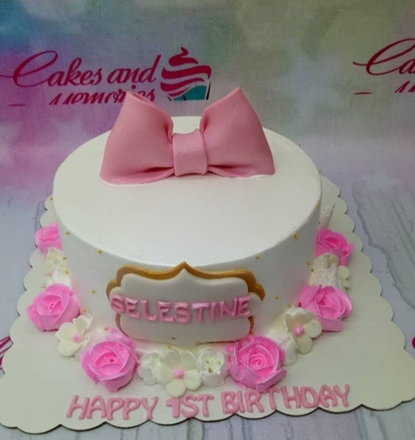 White 1-tier birthday cake with a large pink fondant bow, pink icing roses, and a personalized name plaque. White 1-tier birthday cake with a large pink fondant bow, pink icing roses, and a personalized name plaque.