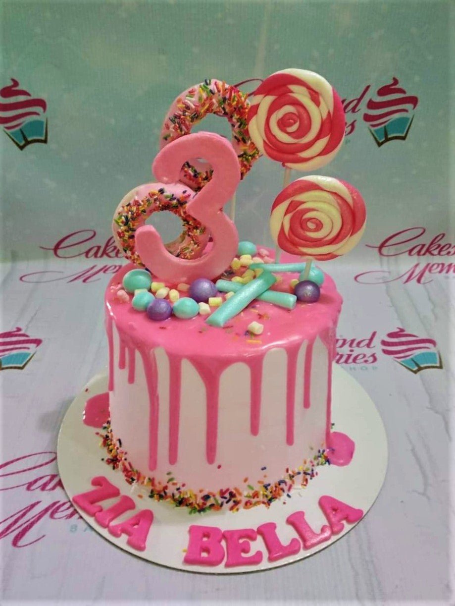 Pink drip cake with donuts, lollipops, and a pink number 3 topper for a 3rd birthday celebration. Pink drip cake with donuts, lollipops, and a pink number 3 topper for a 3rd birthday celebration.