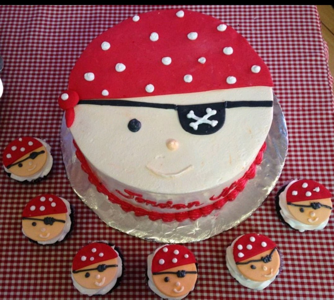 Pirate face cake with red polka dot bandana and black eye patch, surrounded by matching pirate cupcakes. Pirate face cake with red polka dot bandana and black eye patch, surrounded by matching pirate cupcakes.