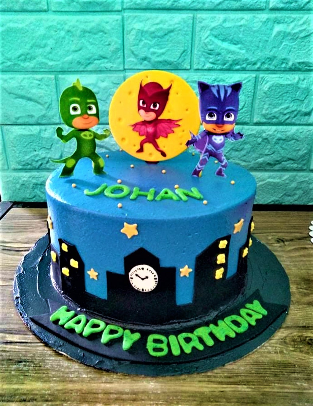 Blue PJ Masks themed birthday cake with Gekko, Owlette, and Catboy toppers and a black city skyline silhouette. Blue PJ Masks themed birthday cake with Gekko, Owlette, and Catboy toppers and a black city skyline silhouette.