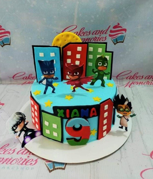 PJ Masks themed blue fondant cake with city skyline toppers, character cutouts, and a large red number 9. PJ Masks themed blue fondant cake with city skyline toppers, character cutouts, and a large red number 9.