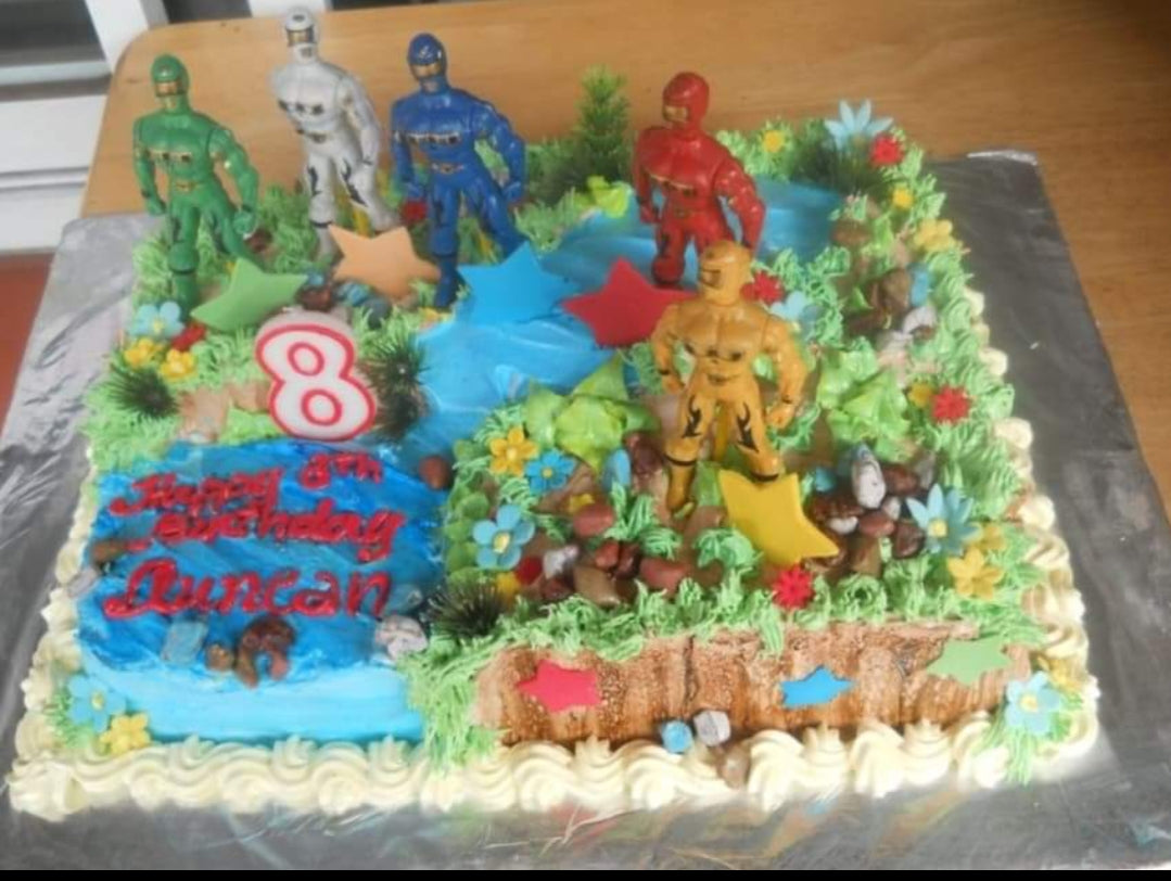 Power Rangers themed rectangle birthday cake with 3D action figures, blue icing river, and green grass piping for Duncan's 8th birthday. Power Rangers themed rectangle birthday cake with 3D action figures, blue icing river, and green grass piping for Duncan's 8th birthday.