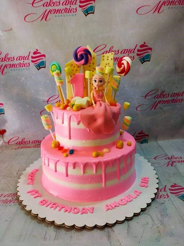 Princess Candy 2-Tier Birthday Cake Pink and white striped 2-tier birthday cake with a princess figurine, lollipops, marshmallows, and pink icing drips.