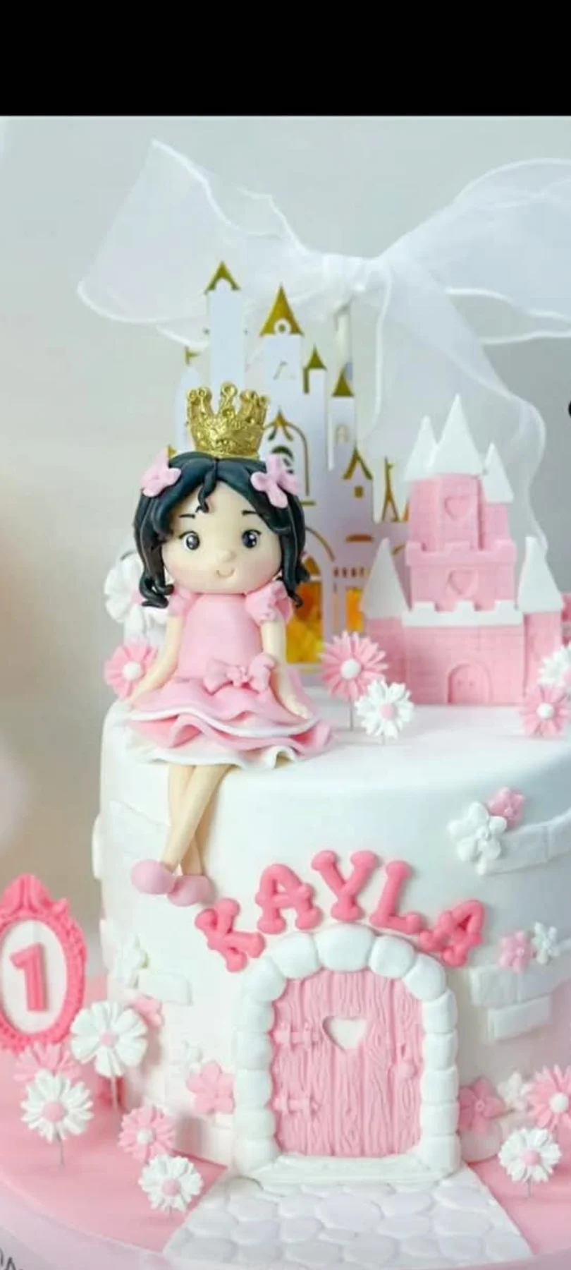 Pink and white princess castle cake with a fondant girl figurine wearing a gold crown and pink dress, surrounded by fondant flowers. Pink and white princess castle cake with a fondant girl figurine wearing a gold crown and pink dress, surrounded by fondant flowers.