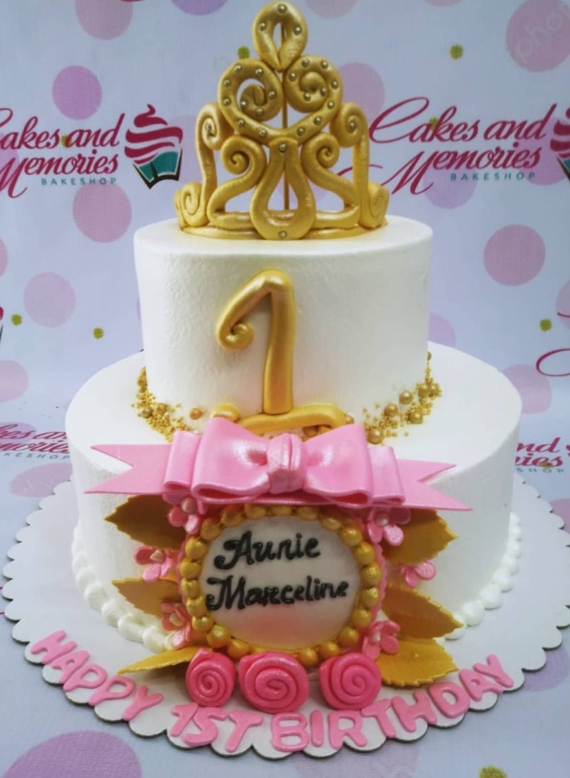 White 2-tier princess birthday cake with a large gold crown topper, pink bow, and gold pearl accents. White 2-tier princess birthday cake with a large gold crown topper, pink bow, and gold pearl accents.