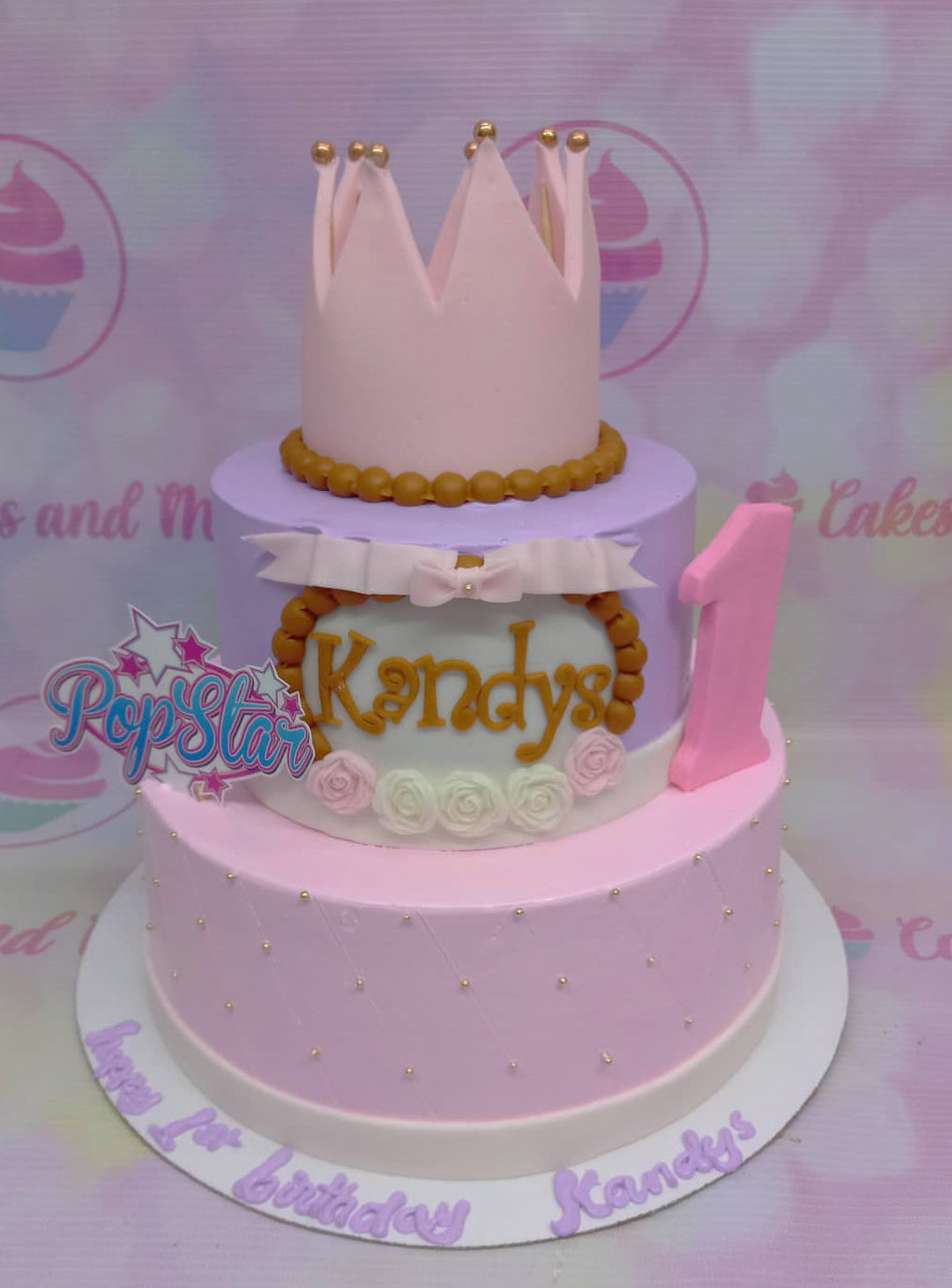 Two-tier pink and purple princess cake with a large pink crown topper, gold bead accents, and a Pop Star printout. Two-tier pink and purple princess cake with a large pink crown topper, gold bead accents, and a Pop Star printout.