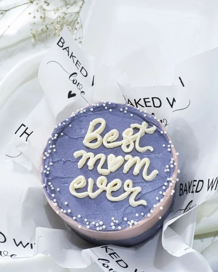 Purple bento cake with white piped icing text saying Best Mom Ever and white pearl sprinkles around the top edge. Purple bento cake with white piped icing text saying Best Mom Ever and white pearl sprinkles around the top edge.