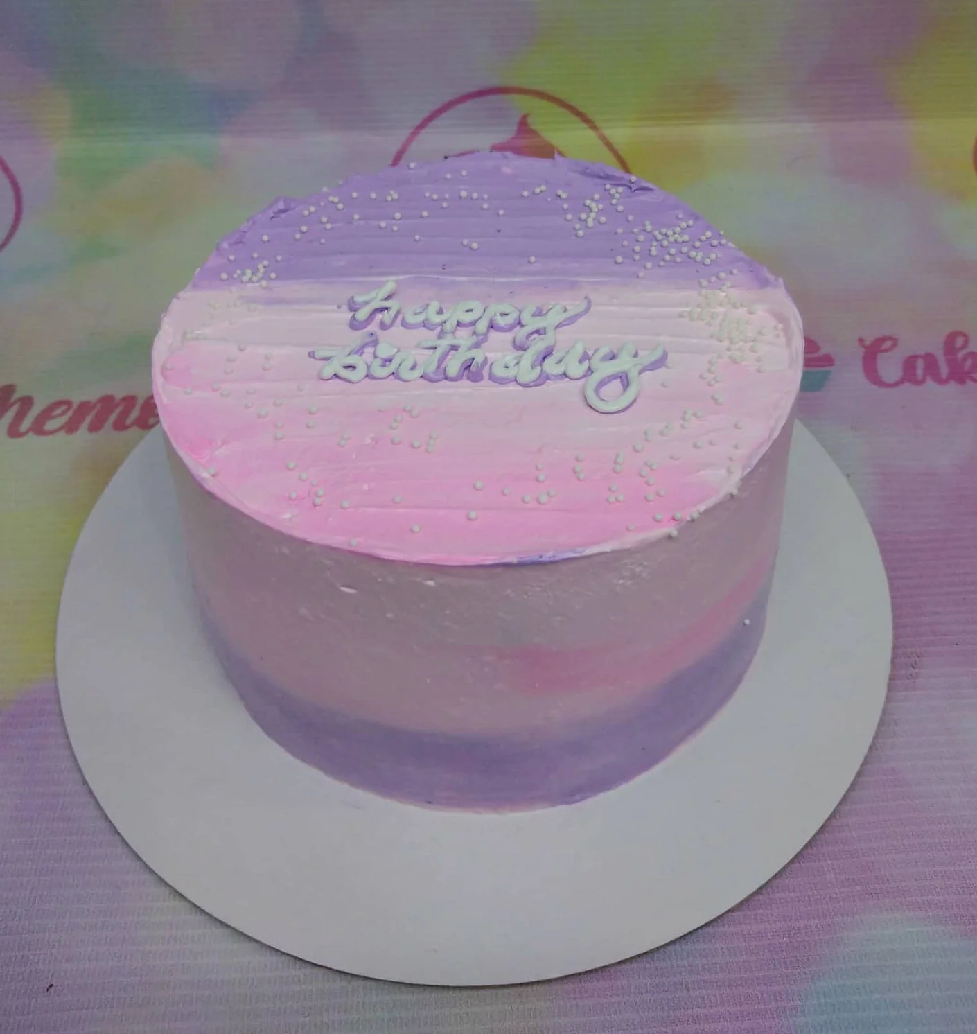 Purple Pink Ombre Sky Blue Birthday Cake A purple and pink ombre 1-tier cake themed around a birthday, featuring a 'Happy Birthday' text topper and white sprinkles.