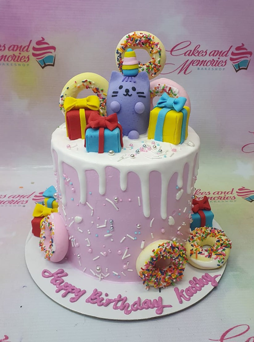 Pink Pusheen cat birthday cake with white chocolate drip, fondant donuts, and colorful gift boxes. Pink Pusheen cat birthday cake with white chocolate drip, fondant donuts, and colorful gift boxes.