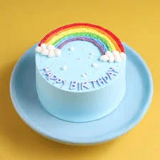 Rainbow birthday colorful cake design — 1 layer soft icing cake in light blue — with Piped rainbow, Piped icing clouds, Piped icing dots, and custom "HAPPY BIRTHDAY" message