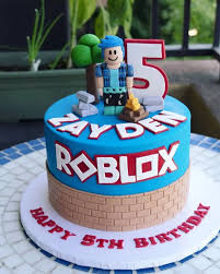 Blue Roblox themed cake with a 3D fondant character, brick wall base, and red Roblox logo. Blue Roblox themed cake with a 3D fondant character, brick wall base, and red Roblox logo.