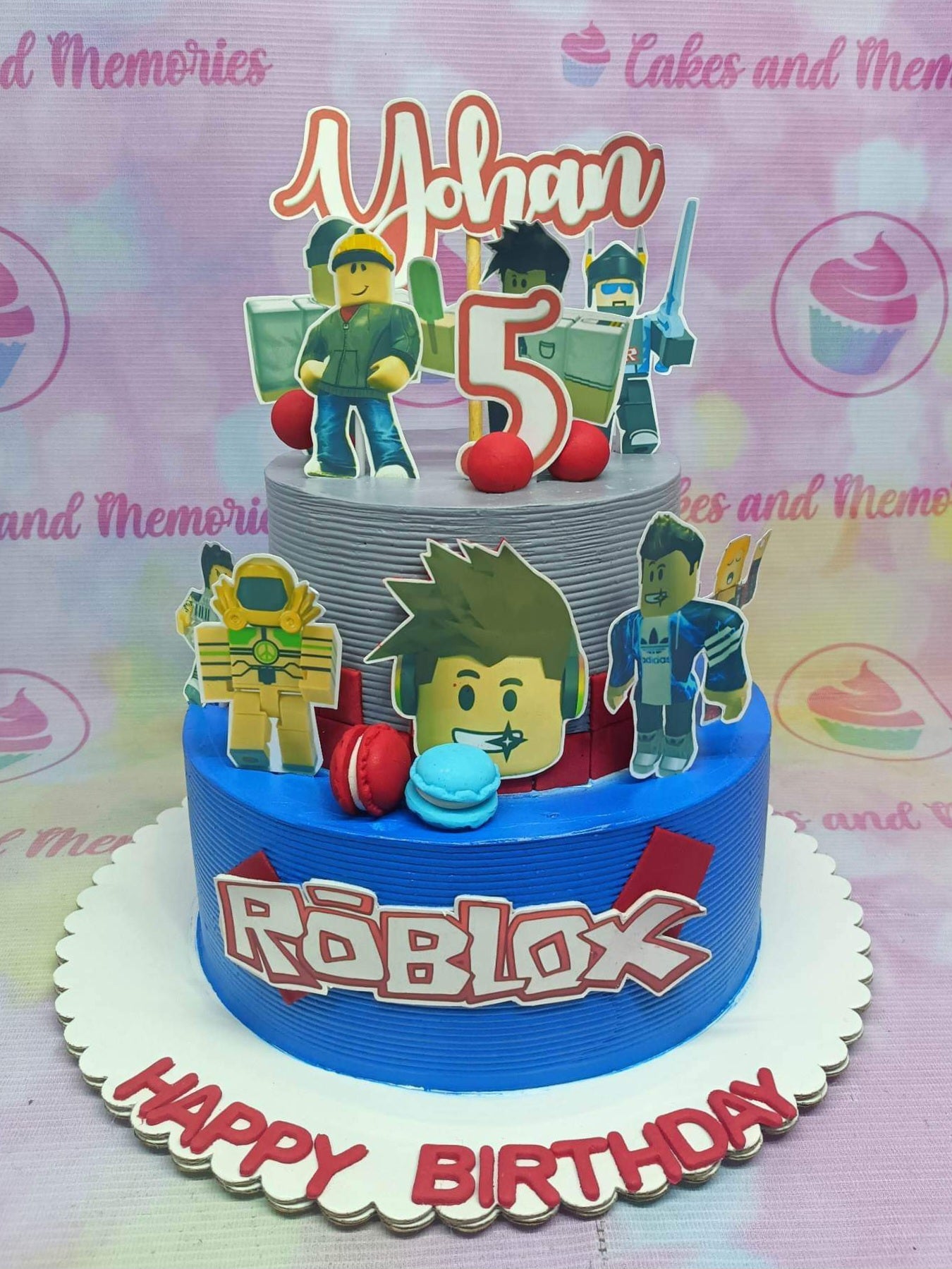 Two-tier Roblox themed birthday cake with blue and gray textured icing, character printouts, and a red Roblox logo. Two-tier Roblox themed birthday cake with blue and gray textured icing, character printouts, and a red Roblox logo.