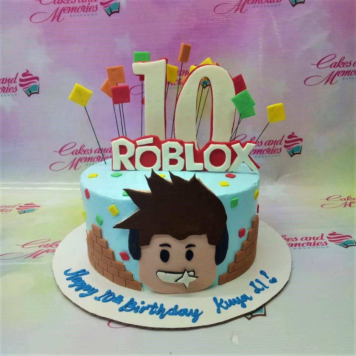 Light blue Roblox themed birthday cake with a large fondant character face, brick wall details, and colorful square accents. Light blue Roblox themed birthday cake with a large fondant character face, brick wall details, and colorful square accents.