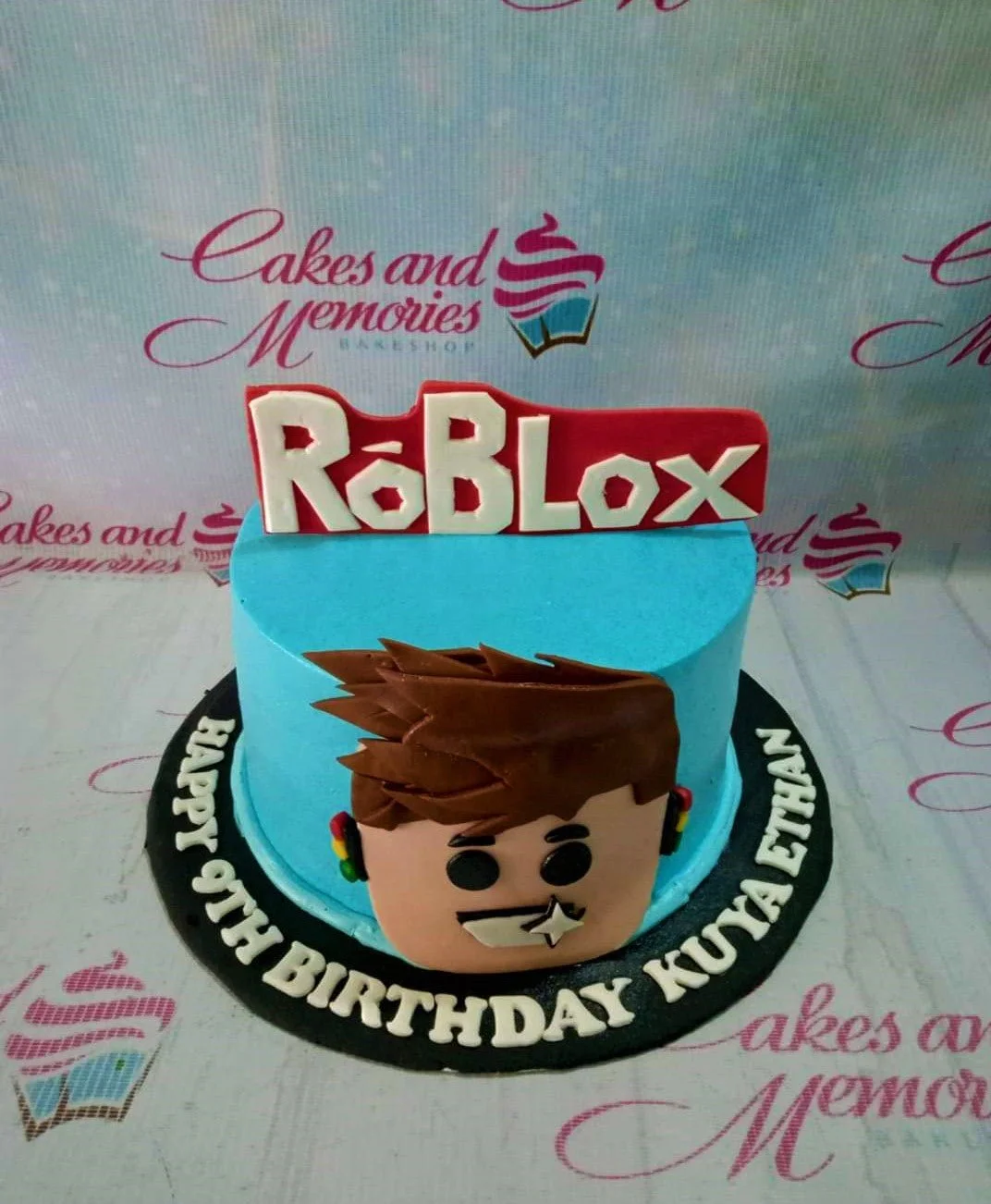 Roblox-Inspired Sky Blue Birthday Cake A light blue 1-tier cake themed around Roblox, featuring a large Roblox logo topper and a 3D fondant character face.