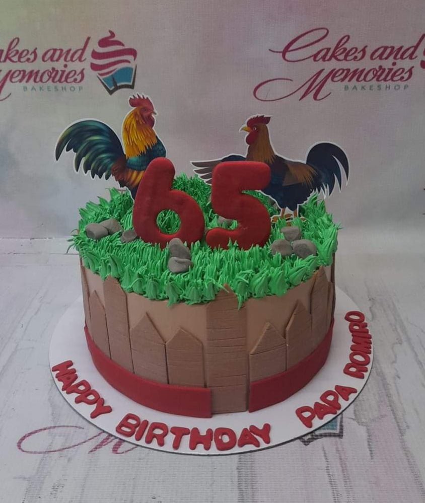 A brown 1-tier birthday cake with green icing grass, a brown fence design, and two rooster printouts with a red number 65 topper. A brown 1-tier birthday cake with green icing grass, a brown fence design, and two rooster printouts with a red number 65 topper.
