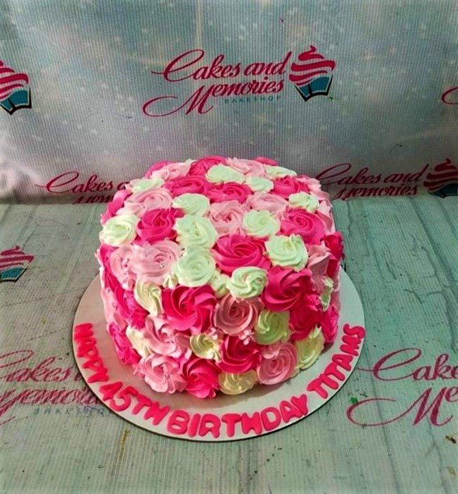 A round single-tier cake covered in pink and white icing rosettes with a birthday message on the base board. A round single-tier cake covered in pink and white icing rosettes with a birthday message on the base board.