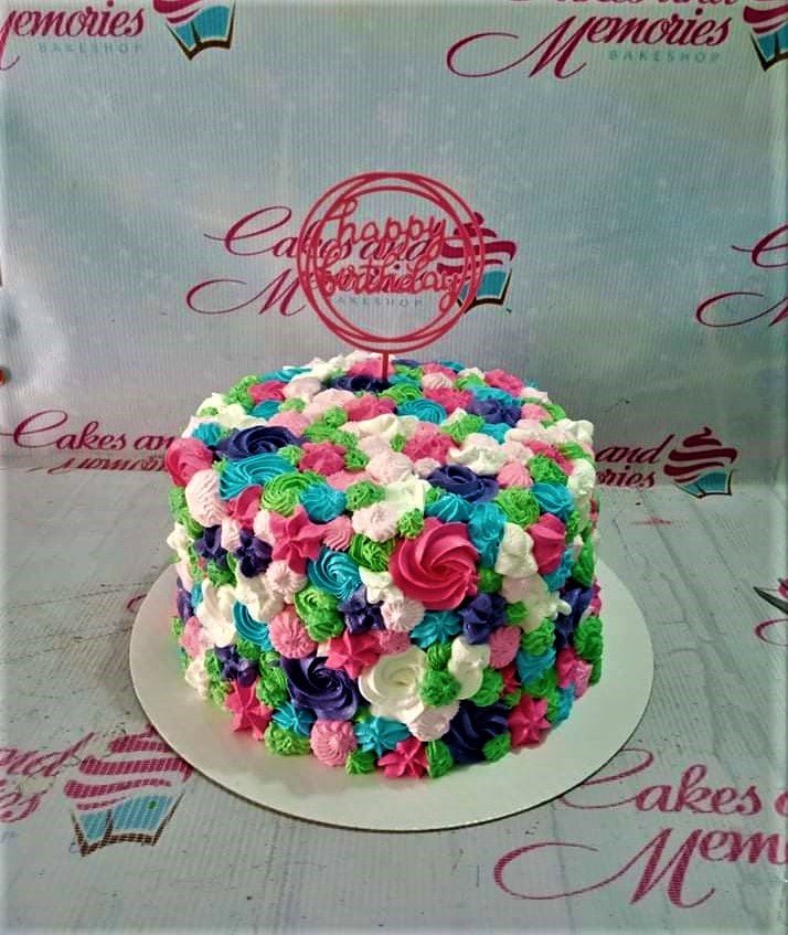 A round cake completely covered in colorful icing rosettes in pink, blue, green, purple, and white with a pink Happy Birthday topper. A round cake completely covered in colorful icing rosettes in pink, blue, green, purple, and white with a pink Happy Birthday topper.