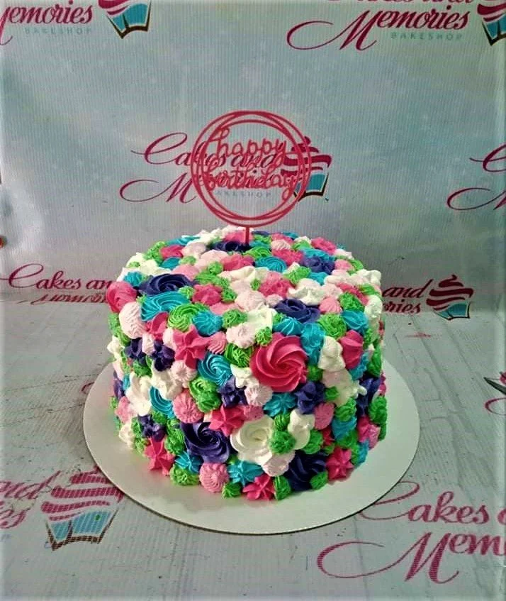 Rosette Birthday Cake A multi-colored 1 Tier round cake themed with Rosettes, featuring a pink 'Happy Birthday' topper and piped icing rosettes.