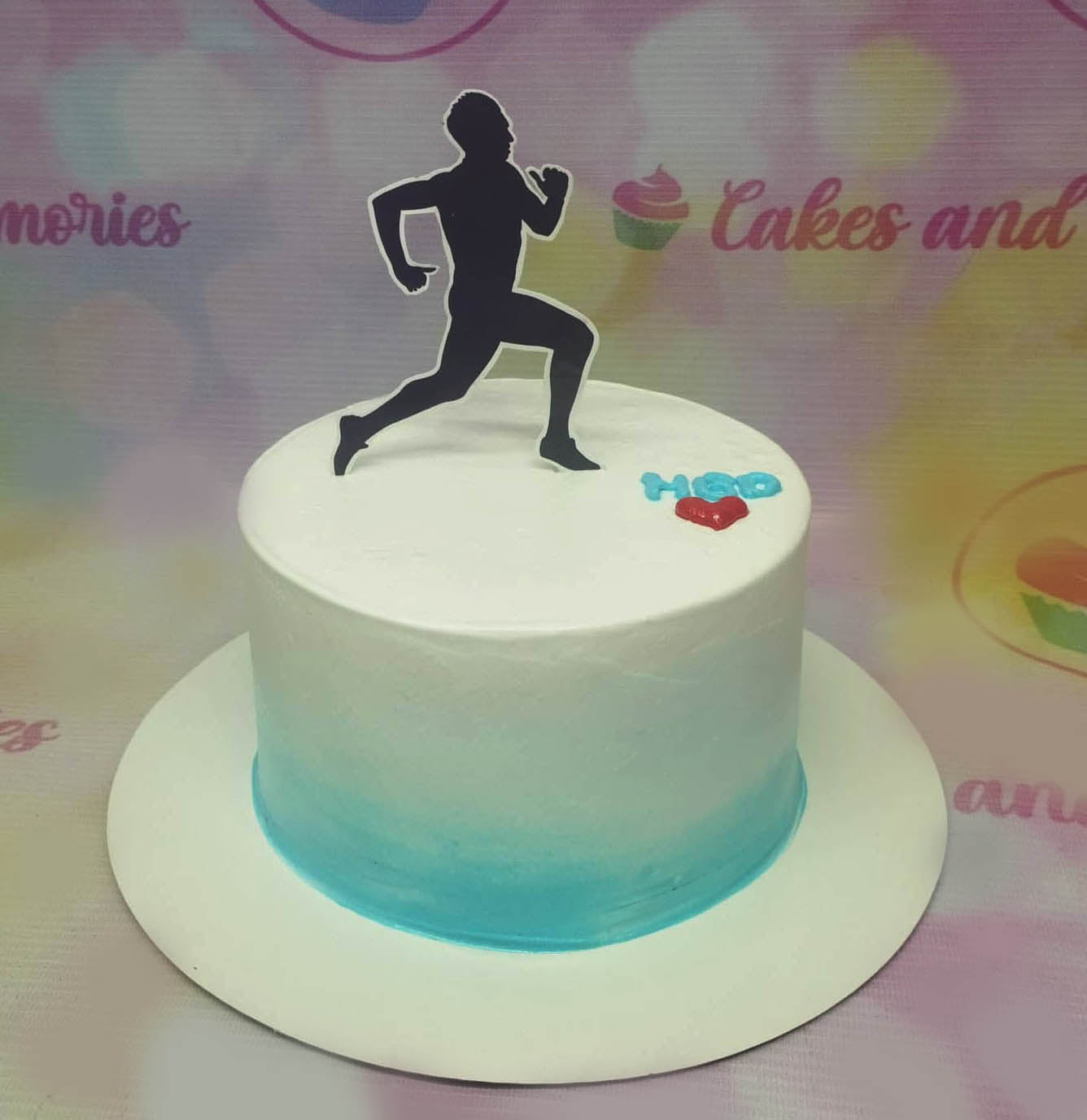 White minimalist cake with a blue gradient base featuring a black runner silhouette topper and a small red heart with HBD text. White minimalist cake with a blue gradient base featuring a black runner silhouette topper and a small red heart with HBD text.