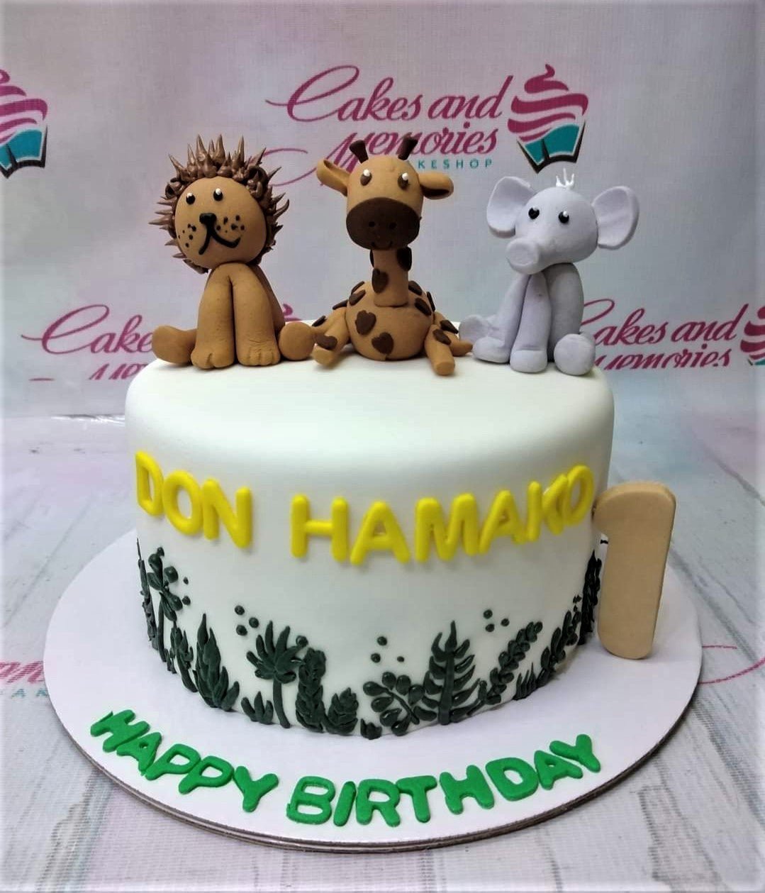 White fondant safari cake with 3D fondant lion, giraffe, and elephant toppers, yellow name letters, and green icing grass. White fondant safari cake with 3D fondant lion, giraffe, and elephant toppers, yellow name letters, and green icing grass.