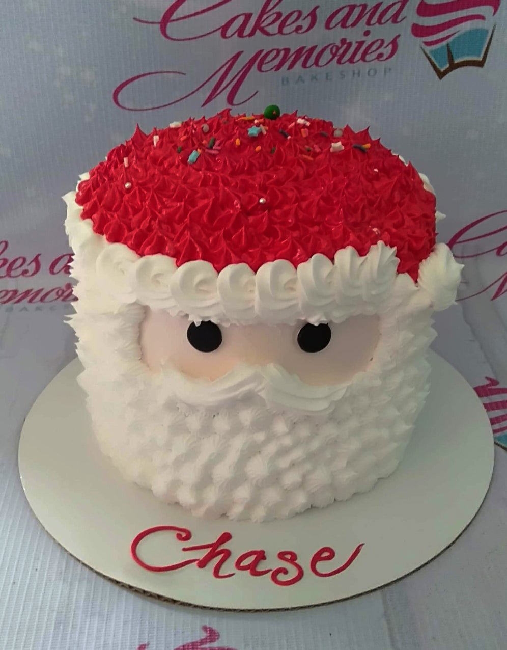 Santa Claus themed cake with red icing hat, white icing beard, and black eyes on a white base board. Santa Claus themed cake with red icing hat, white icing beard, and black eyes on a white base board.