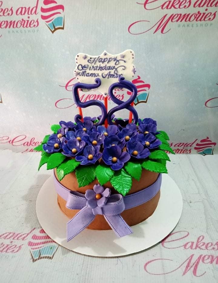 Brown round cake with purple fondant flowers, green leaves, a purple ribbon, and a number 58 topper for Mama Amor's birthday. Brown round cake with purple fondant flowers, green leaves, a purple ribbon, and a number 58 topper for Mama Amor's birthday.