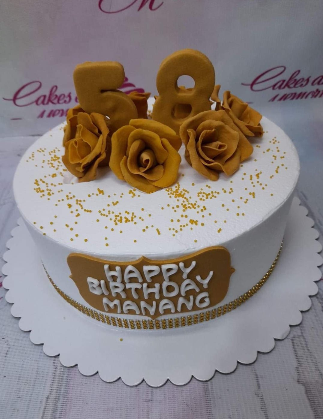 White round birthday cake with gold fondant roses, gold number 58 toppers, and gold sprinkles. White round birthday cake with gold fondant roses, gold number 58 toppers, and gold sprinkles.